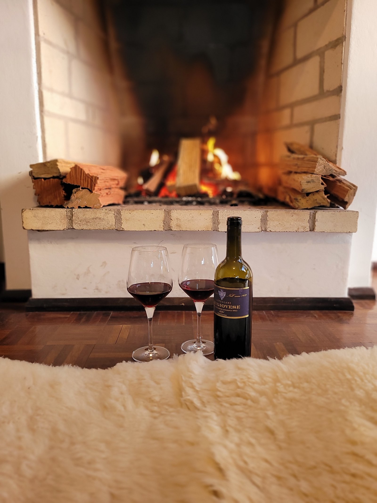 Garrafa de vinho e taças junto à lareira no ambiente da La Bottega